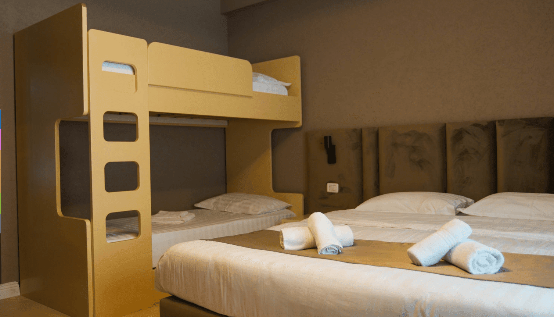 Modern hotel room with bunk beds and a double bed, adorned with neatly folded towels.