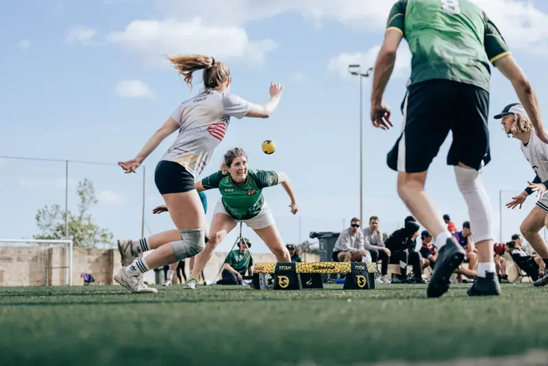 Two women in white and green go for the ball over a roundnet during a rally