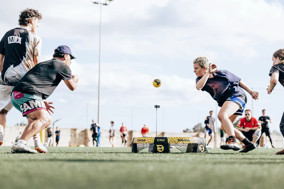 A roundnet rally at FRESH: the ball hangs above the net while a player dives forward and two opponents close in