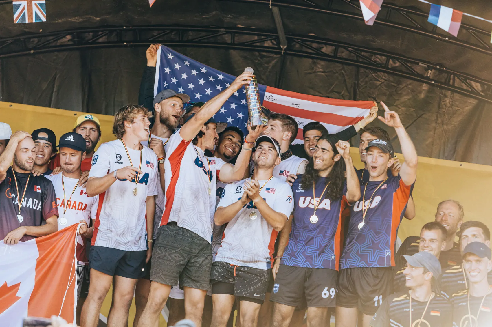 The United States squad celebrating with the trophy and the American flag at the 2022 Roundnet World Championship in Belgium, with Canada in silver to the left and Germany in bronze to the right.